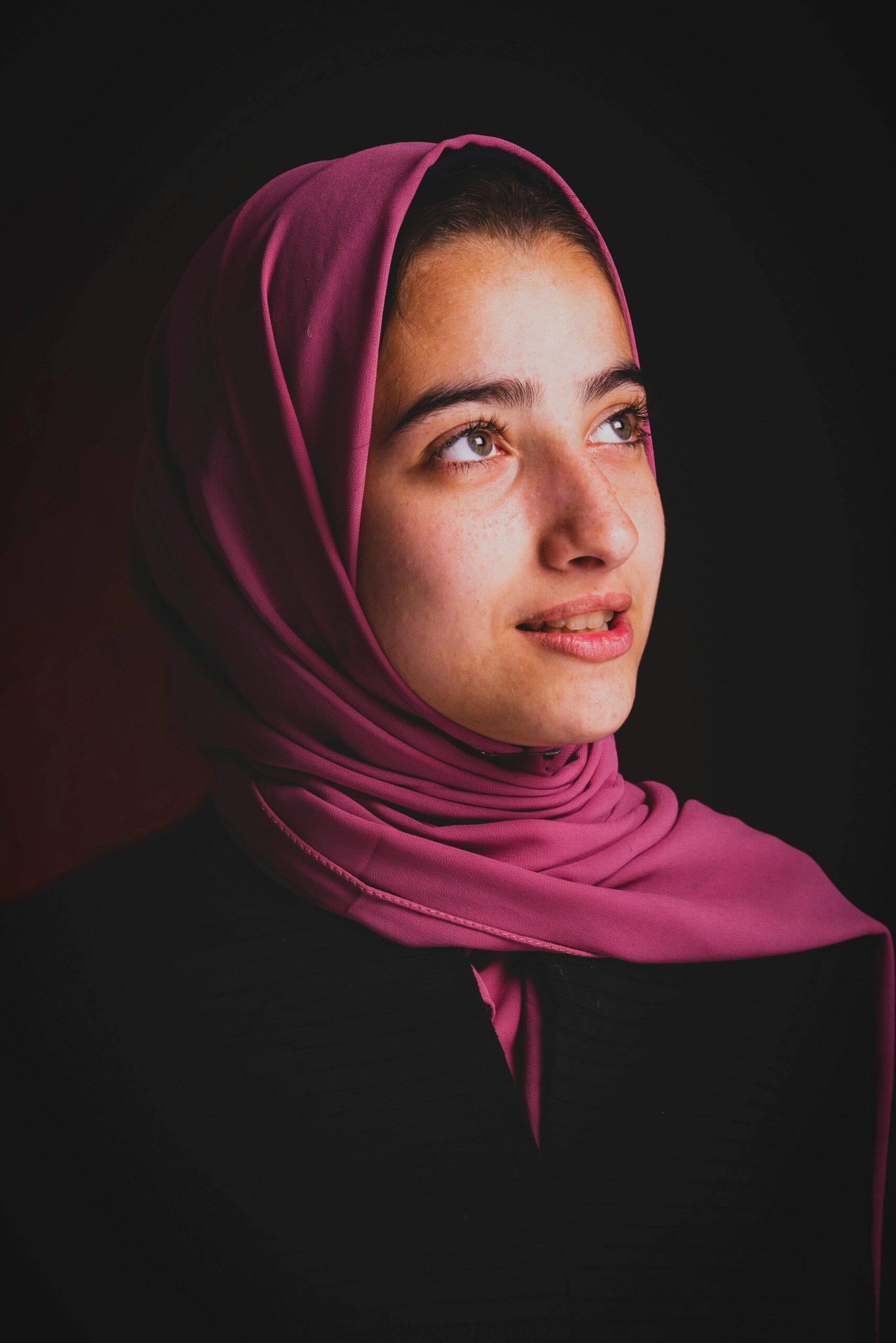 A beautiful portrait of a young woman wearing a pink hijab, captured in a studio setting.