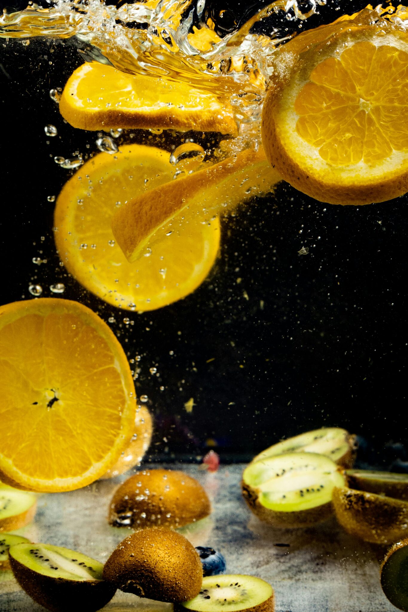 Sliced oranges and kiwis submerge in water, creating a fresh and vibrant splash effect.