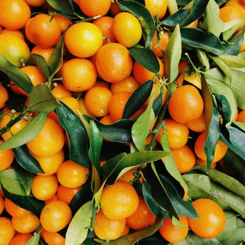 A vibrant pile of fresh tangerines with green leaves, showcasing natural freshness and vivid colors.