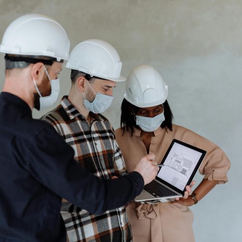 Group of diverse architects with safety gear examining building plans on a laptop.